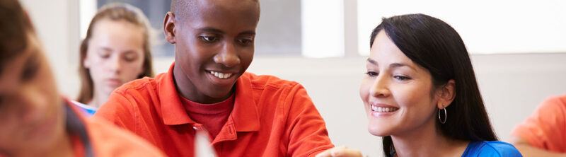 Teacher looks at tablet with student in classroom